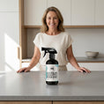 Load image into Gallery viewer, Woman standing behind a kitchen counter with a bottle of Australian Eucalyptus Bench Spray.
